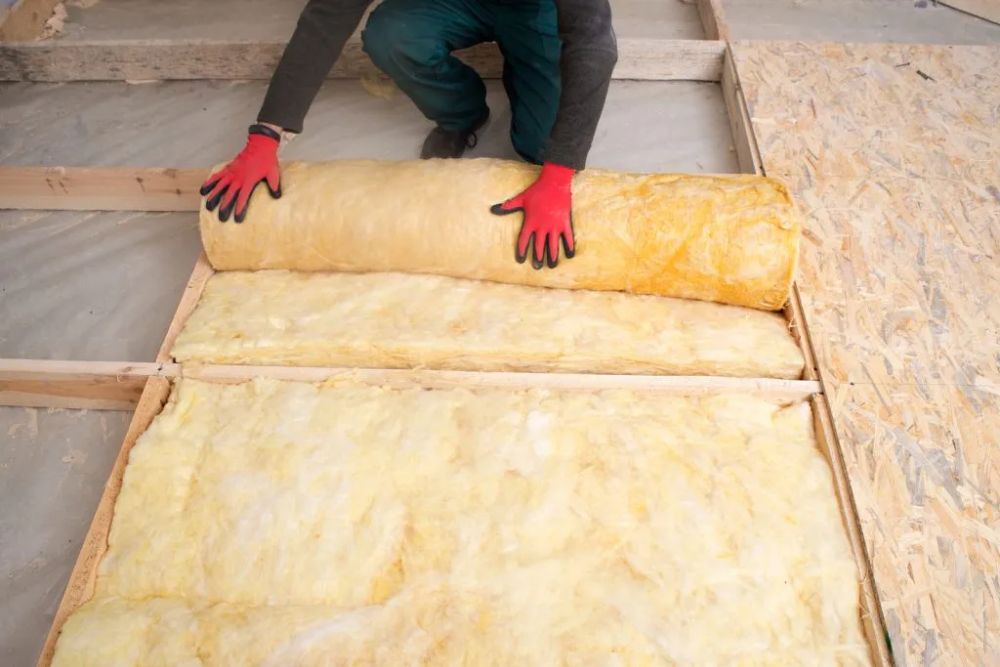 A man is installing insulation material on the floor of a room, focused on his task.