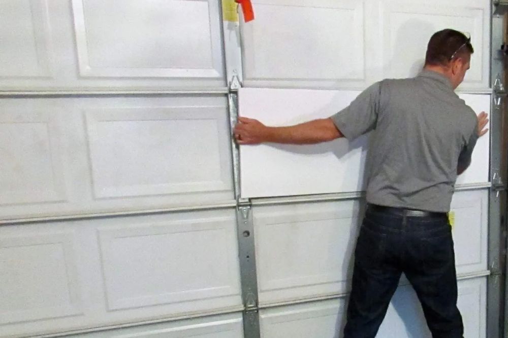 A man works on installing a garage door, focused on the task in a well-lit garage environment.