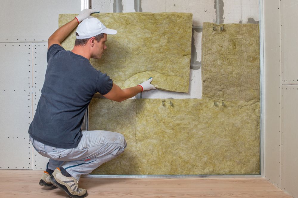 A man works on installing insulation in a room, ensuring proper coverage for improved thermal performance.
